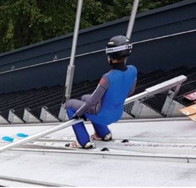 Bild eines Skispringers; der Springer trägt einen blauen Anzug, einen Helm und Ski und ist beim Start auf der Piste zu sehen