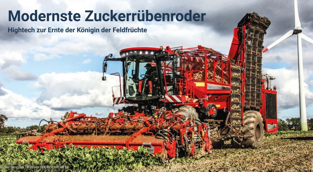 Der große rote Zuckerrübenroder Terra Dos T4-30 von HOLMER während der Fahrt auf einem Feld; rechts im Hintergrund bewölkter blauer Himmel und ein Windrad