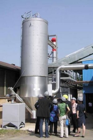 Eine Gruppe von Menschen mit Bauhelmen steht vor einem großen silbernen Klärturm (die AshDec®-Pilotanlage)