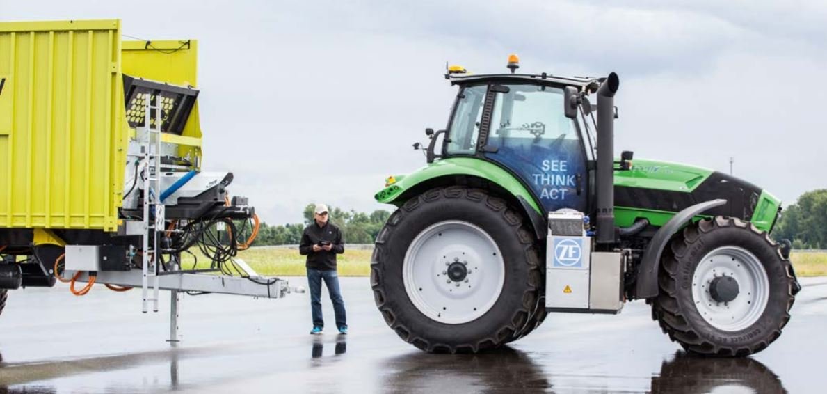 Foto des großen Innovations-Traktor von ZF mit grüner Außenlackierung, links daneben ein Mann und ein gelber Container