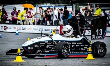 Fahrzeug der Formula Student Electric mit Fahrer, der einen Helm trägt, auf einer Rennstrecke; im Hintergrund Zuschauer