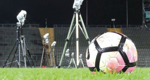 Das Innere eines Stadions mit einem Fußball im Vordergrund, im Hintergrund sind Stative und eine Tribüne zu sehen