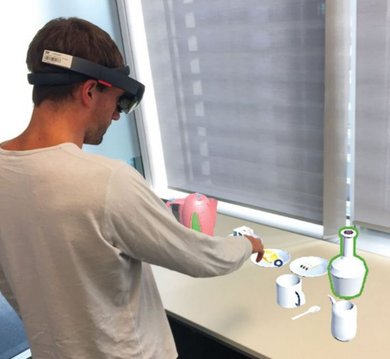 Mann mit HoloLens vor auf einem Tisch eingeblendeten virtuellen Elementen