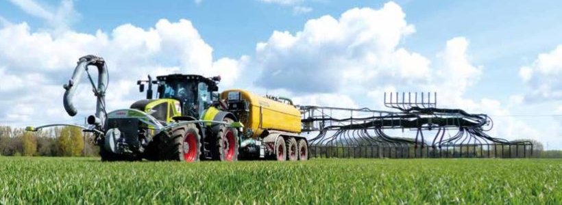 Traktor mit angehängtem Güllefass auf einem grünen Feld