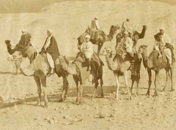 Sepiafarbenes Bild mit sieben Kamelen in der Wüste, auf denen Männer sitzen